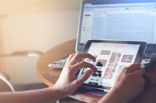 Una persona usando una tableta electrónica con un portátil de fondo