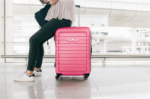 Viajera esperando vuela apoyada en maleta rosa