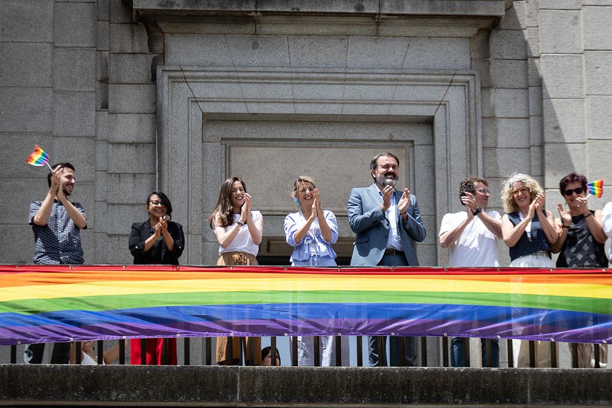 Yolanda Díaz y representantes de la Federación Estatal LGTBI+ aplauden tras desplegar la bandera multicolor.